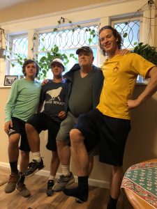 four men standing arms linked, one leg raised.