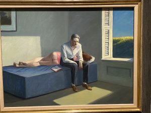 Man sitting at edge of bed with woman asleep behind him.