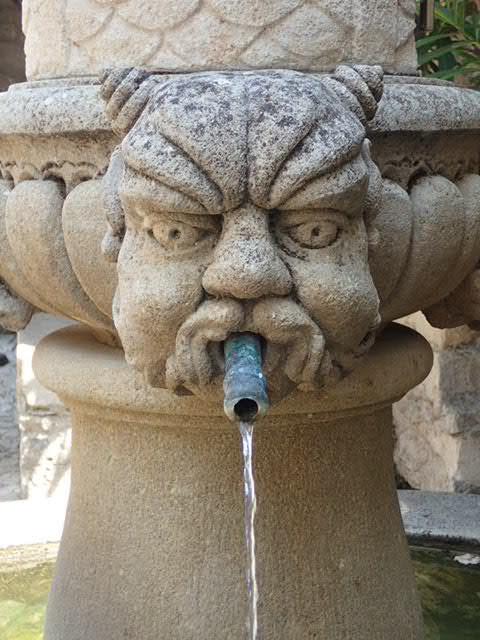 Face on a water fountain with pursed lips around a pipe with water pouring out.
